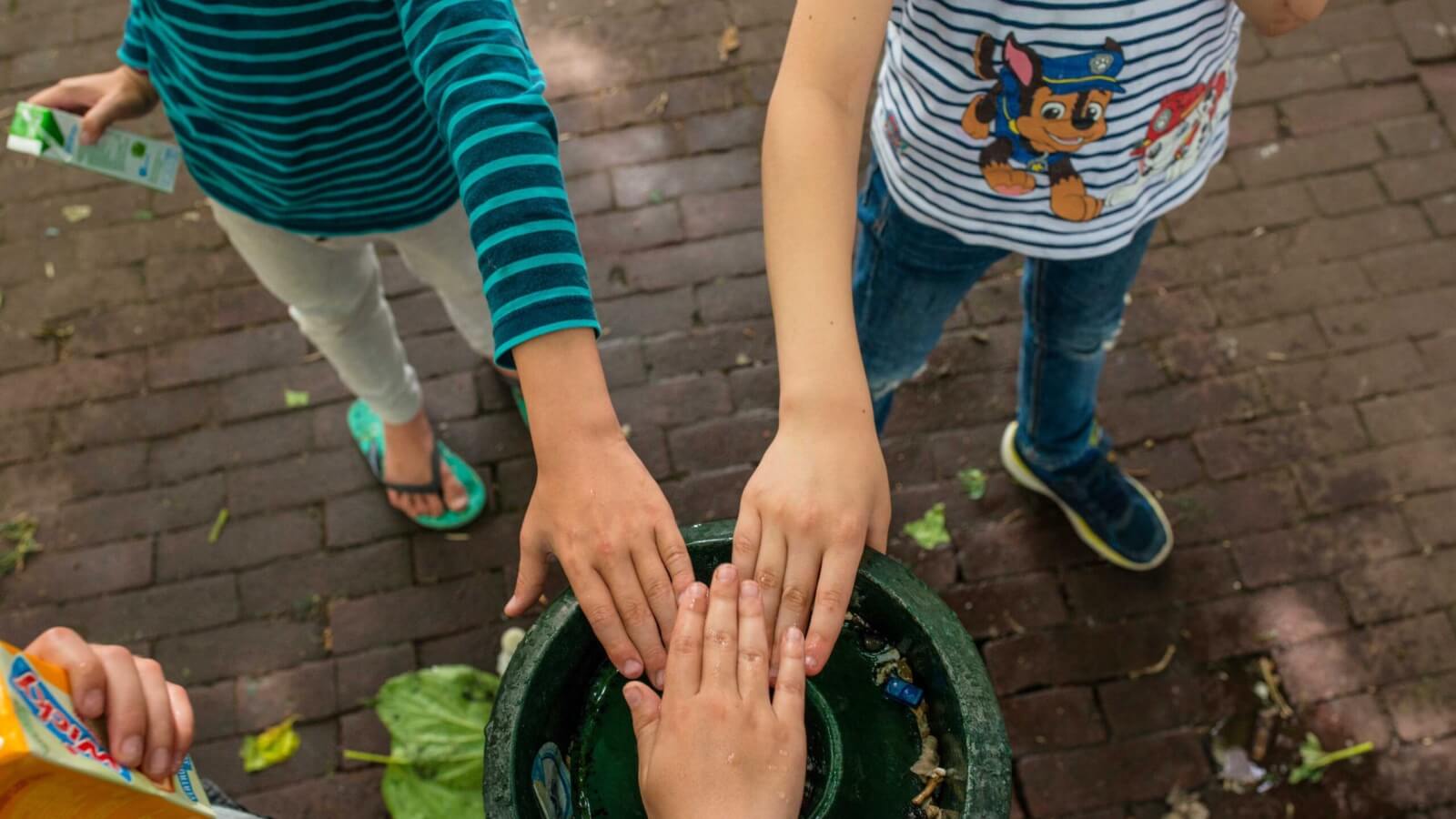Kinderen steken handen bij elkaar op plein basisschool tijdens buitenspelen